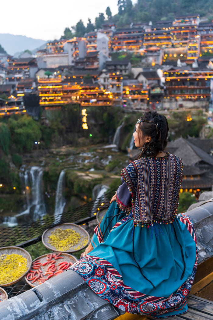 Mujer con vestido azul sentada y observando la ciudad de lijiang